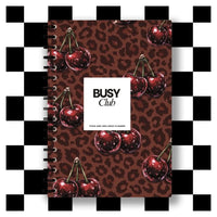 Notebook with cherry design and 'BUSY Club' branding on a checkered background