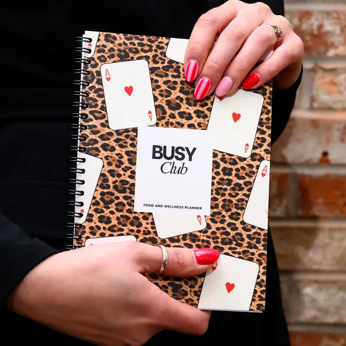Notebook with a leopard print cover featuring playing card designs held by hands.