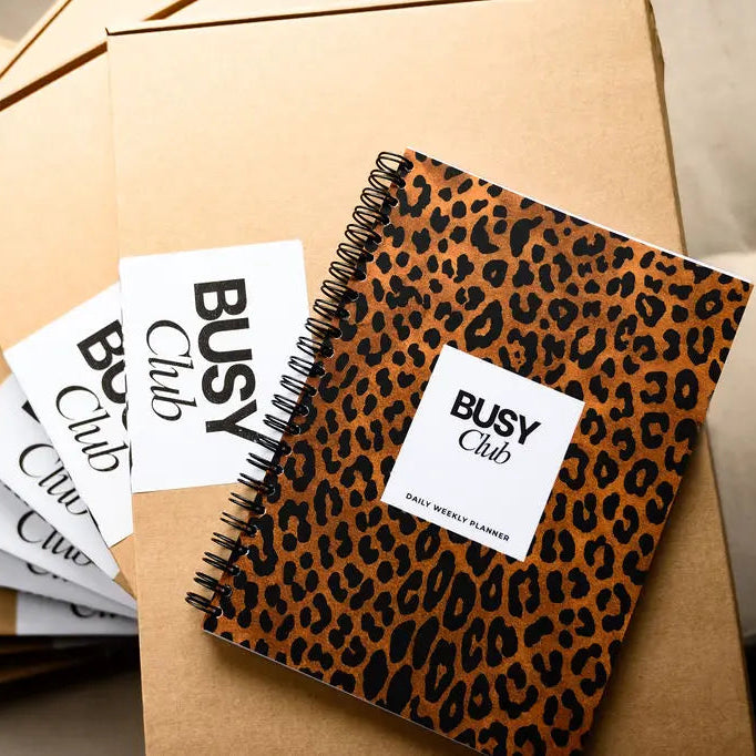 Leopard print notebook with 'Busy Club' branding on a beige surface