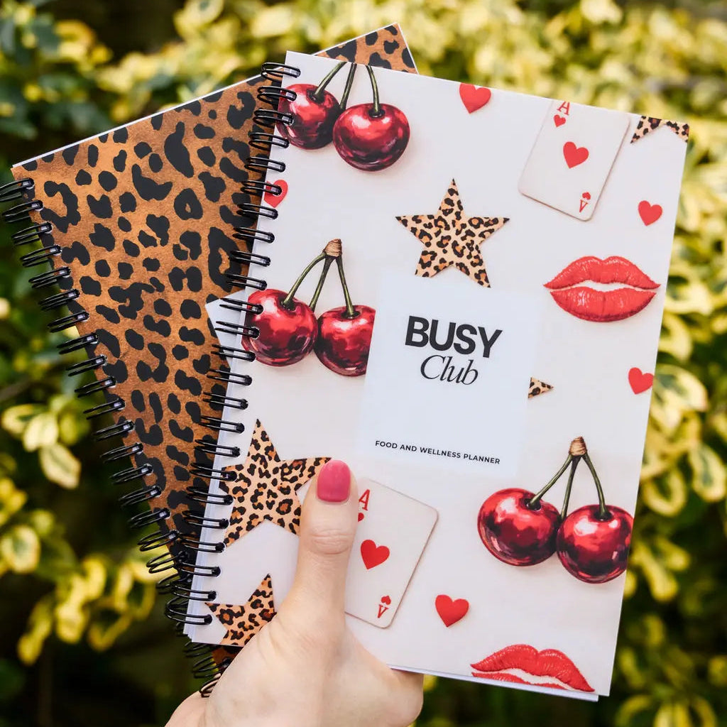 Two notebooks with leopard print and cherry design held against a green leafy background