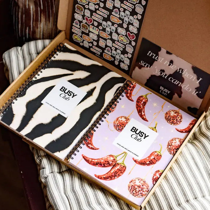 Open box containing notebooks with zebra and chili pepper designs, on a textured surface.