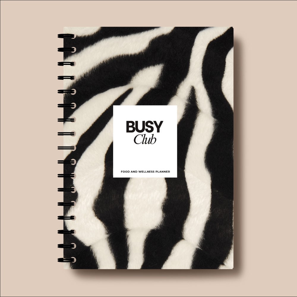 Notebook with zebra pattern cover and 'Busy Club' branding on a beige background