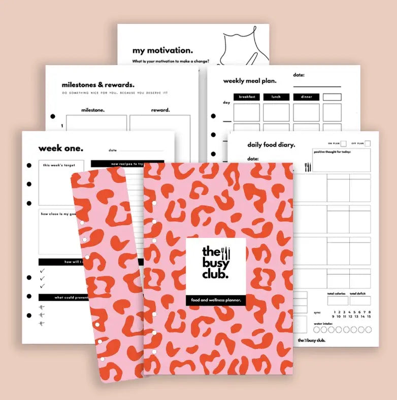 Pink planner with orange pattern and 'the busy club' branding, surrounded by printed sheets on a beige background.