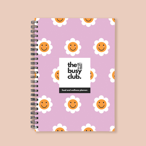 Notebook with 'the busy club' branding and smiley face design on a pink background