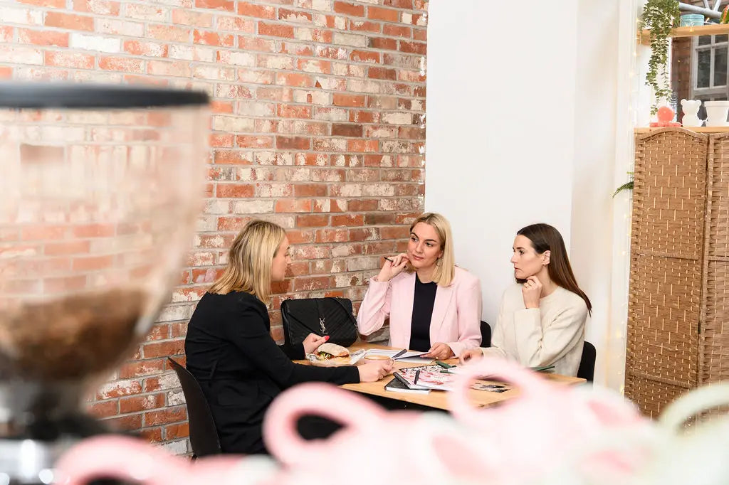 Three women sitting at a table in a casual setting with a brick wall in the background